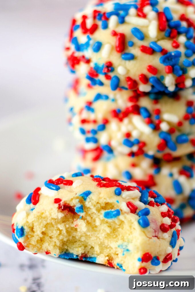 patriotic sprinkle cookies stacked in the background with the one in the front having a bite taken out of it