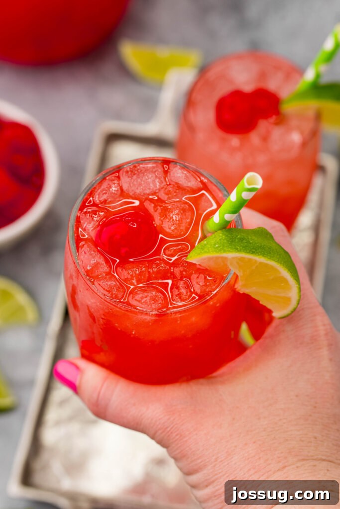 Homemade Sonic Cherry Limeade 3 A hand holding a frosty glass of homemade Sonic Copycat Cherry Limeade, highlighting its vibrant color and icy texture, ready to be enjoyed.