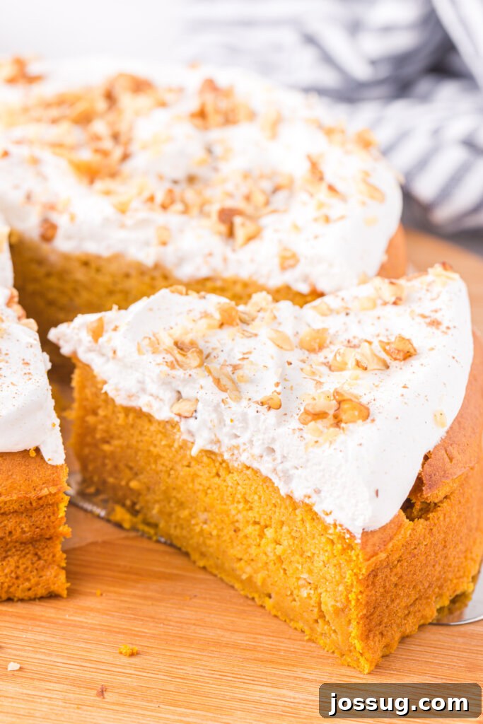Slice of moist pumpkin cake on a plate, adorned with whipped topping and a sprinkle of cinnamon