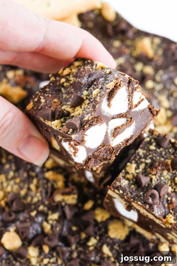 A hand holding a perfectly cut piece of S'mores Fudge, showing its creamy texture and visible inclusions.