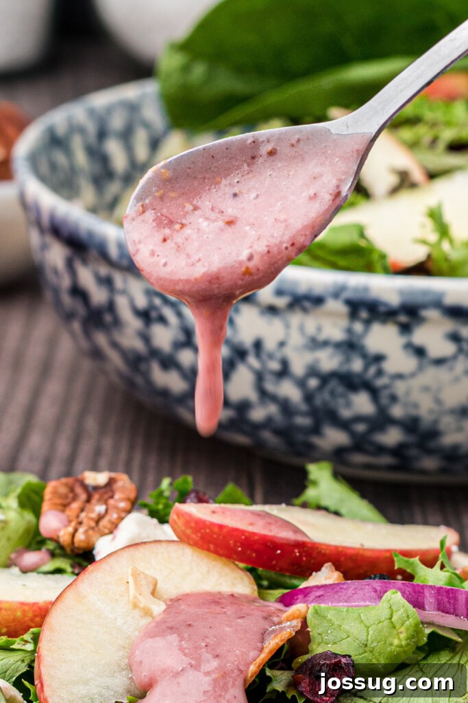 pouring cranberry vinaigrette off spoon onto salad
