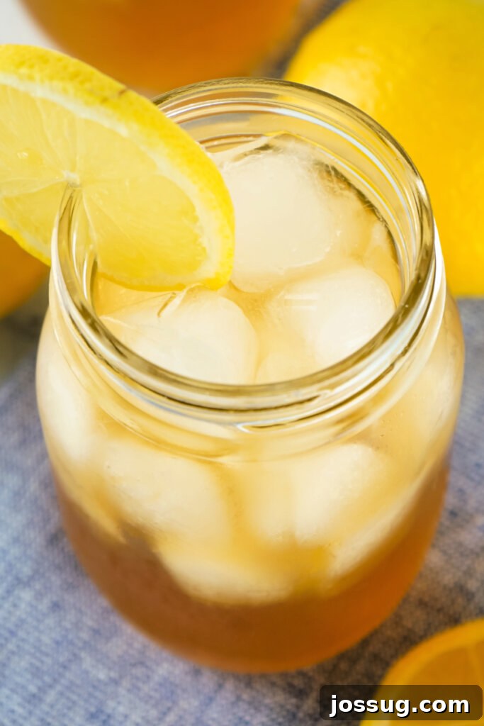 A tall glass filled with amber Spiked Arnold Palmer cocktail, garnished with a vibrant lemon slice, showcasing the refreshing blend.