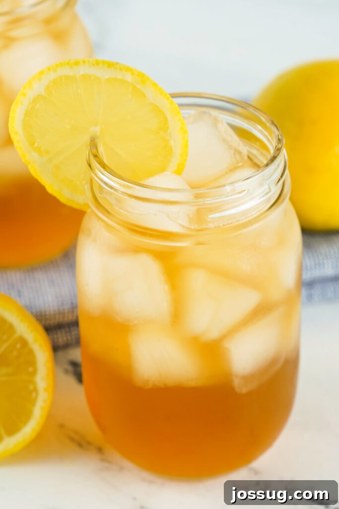 A close-up of a Spiked Arnold Palmer cocktail garnished with a fresh lemon wheel, showing ice and the vibrant color of the drink.