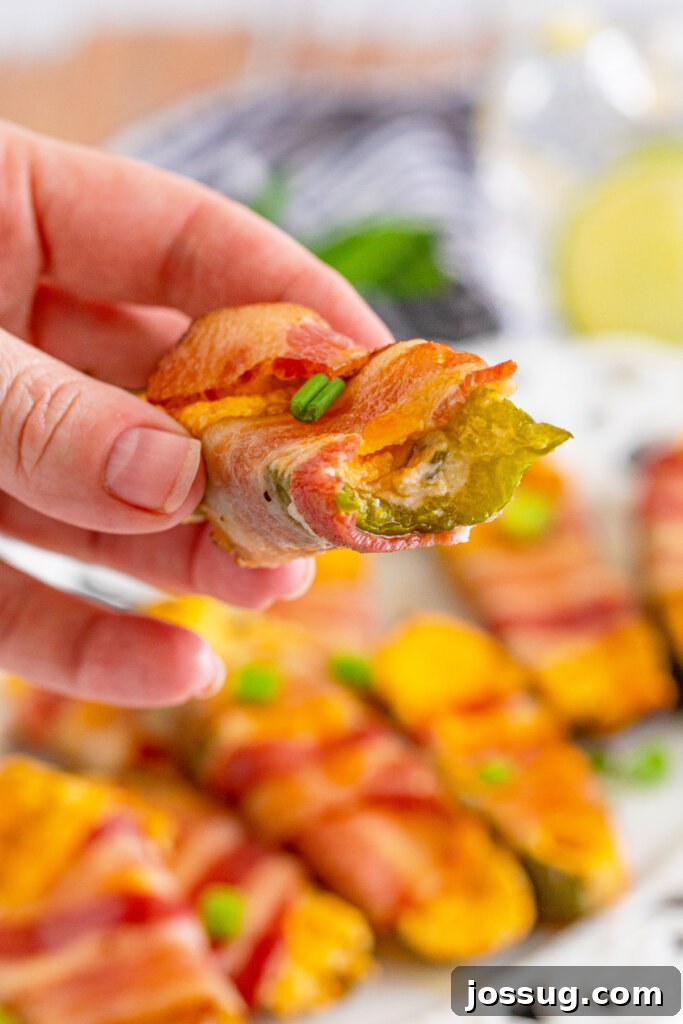 Hand holding a partially eaten bacon-wrapped jalapeno popper, showing the creamy filling