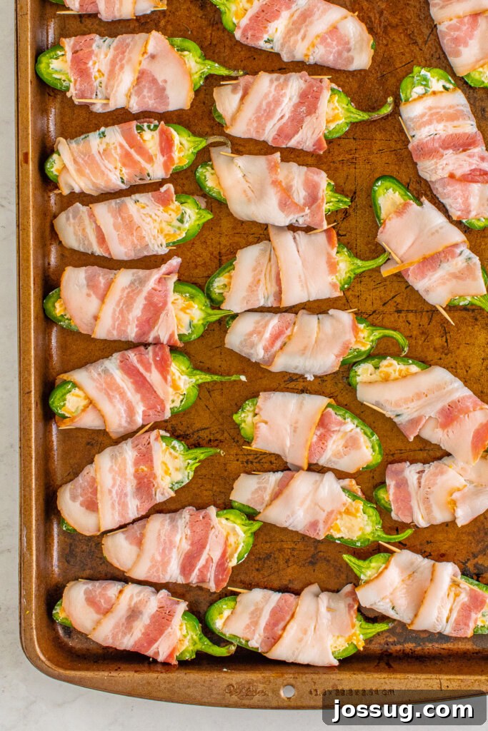 Bacon-wrapped jalapeno poppers arranged on a baking sheet before cooking