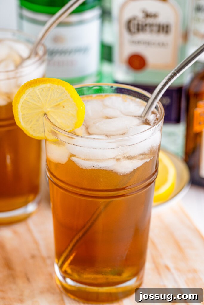 Long Island's Potent Mirage 2 Long Island Iced Tea in a tall glass with alcohol bottles blurred in the background, suggesting a home bar setting.