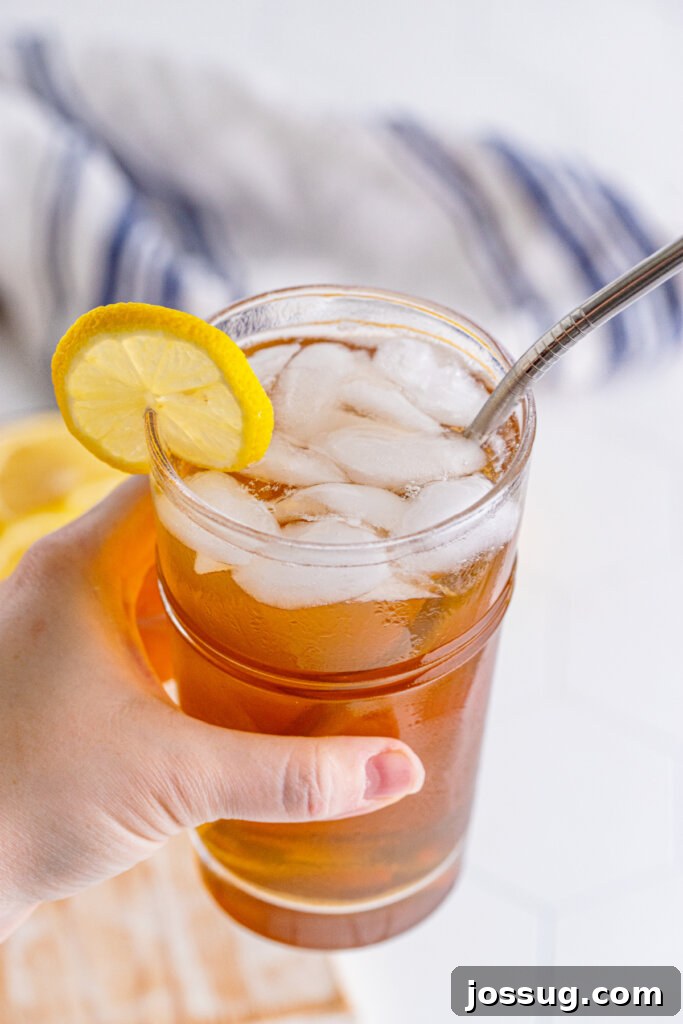 Long Island's Potent Mirage 3 A hand holding a tall glass of Long Island Iced Tea, garnished with a lemon slice, against a bright background.