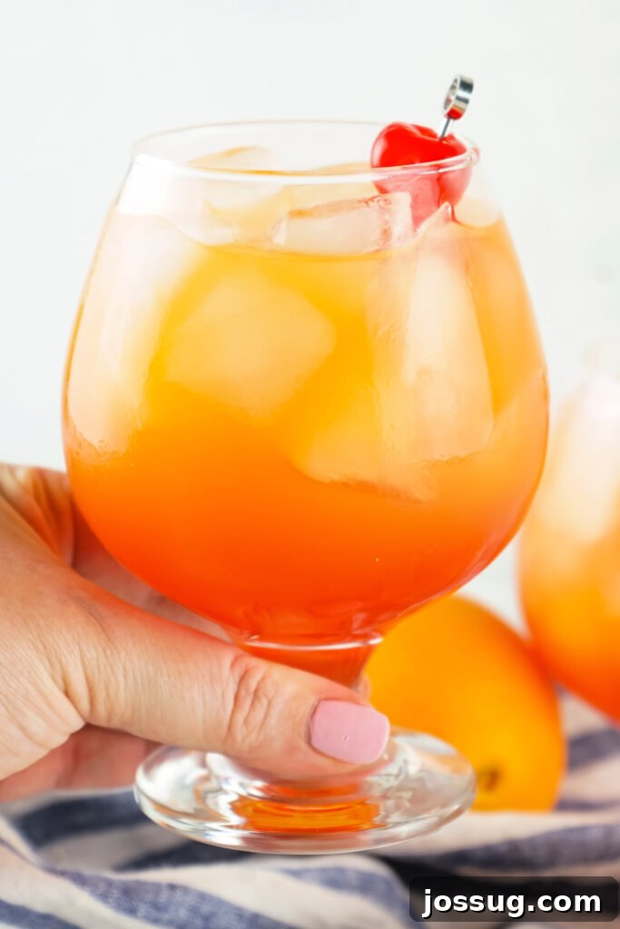 Coastal Rendezvous Cocktail 5 A hand holding a Sex on the Beach cocktail in a tall glass, with a view of a beach in the background