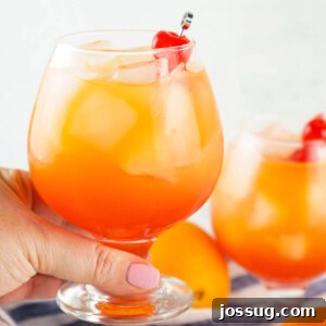 Hand holding a Sex on the Beach cocktail glass with a maraschino cherry garnish