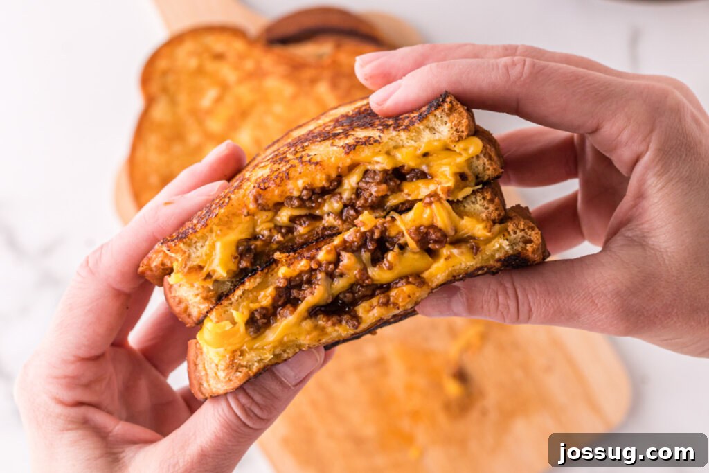 Sloppy Joe Meltdown 5 Hands holding two halves of a cheesy Sloppy Joe Grilled Cheese, ready to be enjoyed.