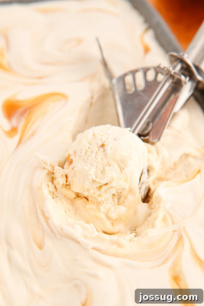 An ice cream scoop diving into a container of perfectly swirled No-Churn Salted Caramel Ice Cream, showcasing its creamy texture.