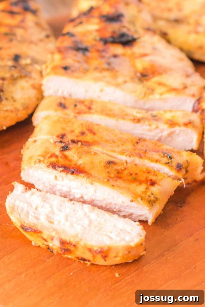 Close-up of juicy sliced honey mustard chicken breast on a wooden board, showcasing a beautiful golden char and tender interior. Garnished with fresh parsley, it's ready to be served.