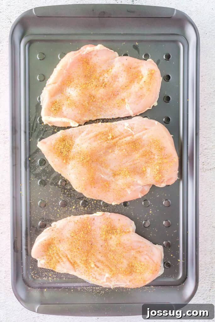 Chicken breasts generously coated with a savory dry spice rub, resting on a marinade tray, ready for the next step of flavor infusion.