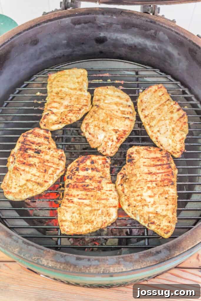 Sizzling chicken breasts cooking on the grill, displaying tantalizing char lines and a golden-brown crust, indicating they are nearly cooked to perfection.