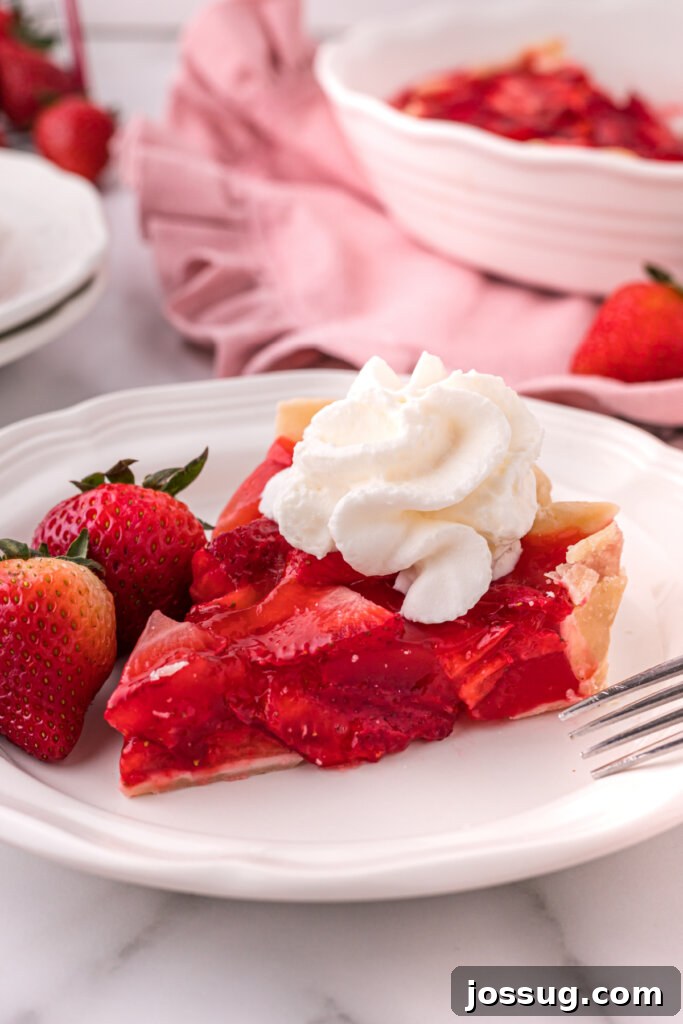 A beautiful slice of fresh strawberry pie on a white plate, showcasing its vibrant red filling and golden crust, ready to be enjoyed.