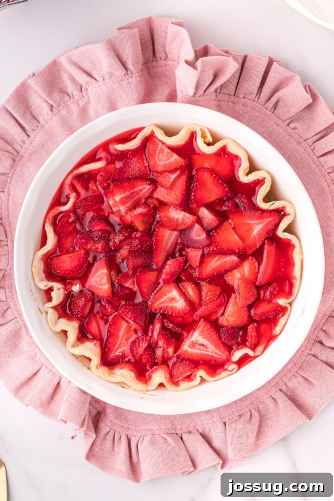 An overhead view of a whole fresh strawberry pie, glistening with its gelatin glaze and piled high with ripe strawberries, ready for slicing.