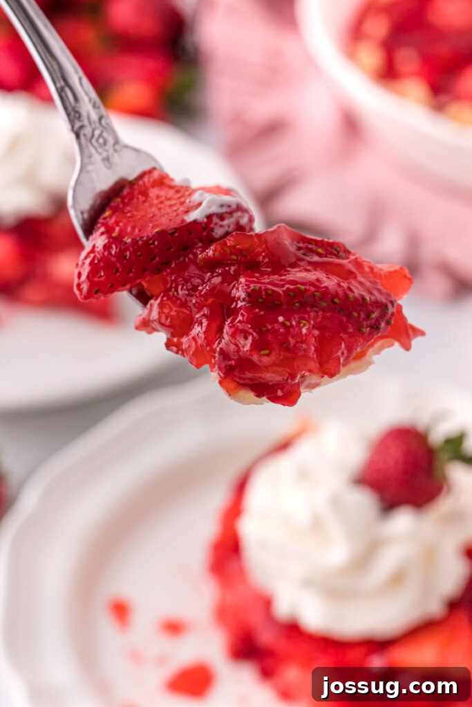 A fork holding a perfect bite of strawberry pie, showing the layers of fresh fruit, glossy glaze, and flaky crust.