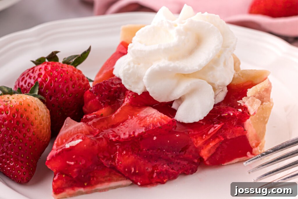 A close-up shot of a single slice of strawberry pie on a plate, highlighting the luscious fresh strawberries and glossy red glaze.