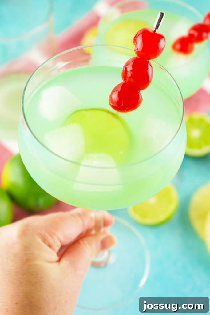 Marine Dream Elixir 4 A hand holding a glass of the Tipsy Mermaid Cocktail, sparkling blue, against a bright background.