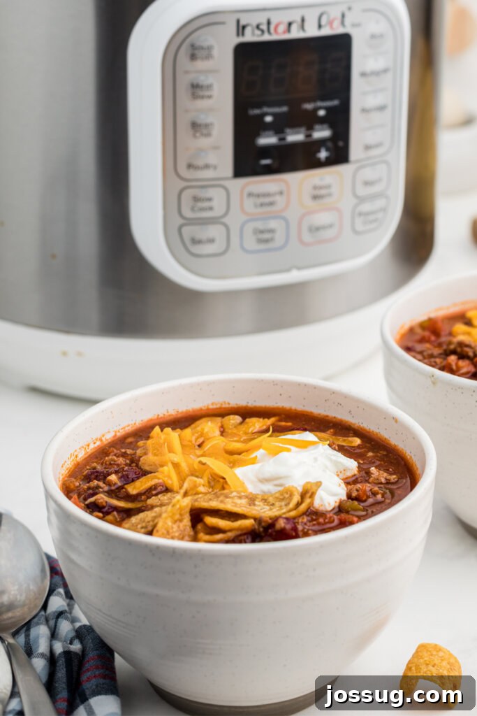 Quick-Fix Instant Pot Chili 3 A bowl of steaming chili topped with cheese and green onions, positioned in front of a gleaming Instant Pot.
