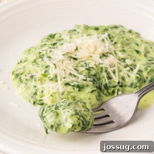 A serving of creamed spinach being lifted with a fork from a bowl, showcasing its creamy texture.