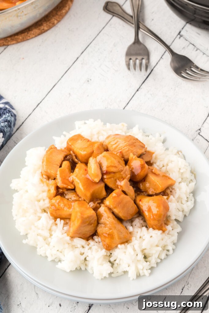 Bourbon Chicken served over fluffy white rice on a plate, garnished with green onions.