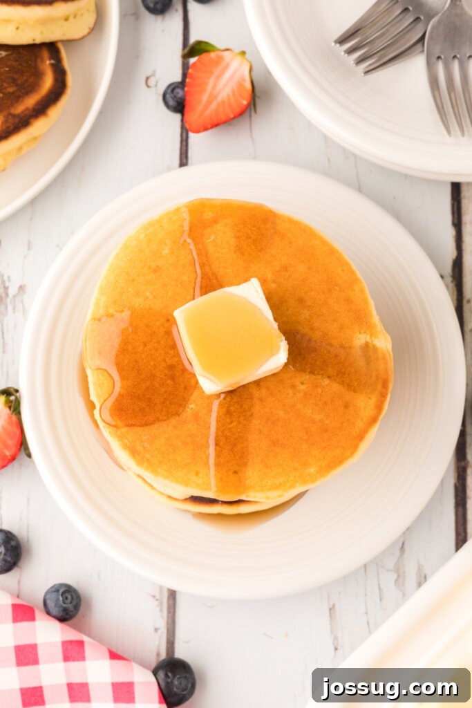 Close-up of fluffy buttermilk pancakes topped with a melting pat of butter and golden maple syrup
