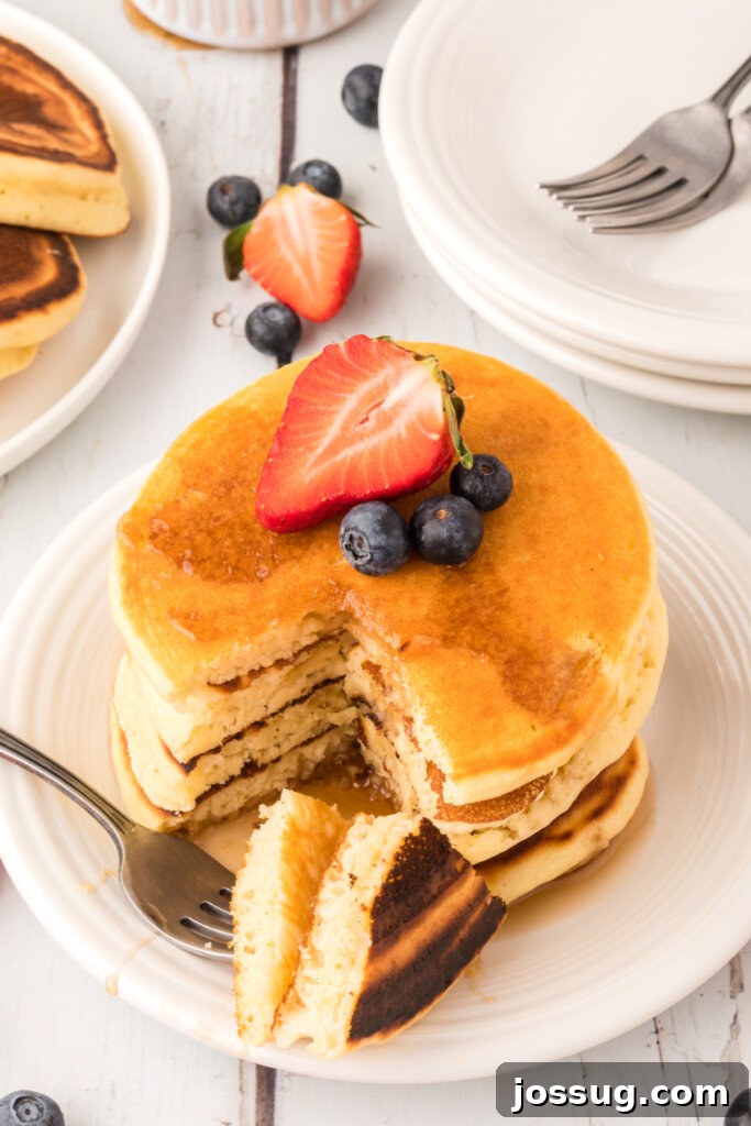 Close-up of a buttermilk pancake with a fork taking a bite, showing the fluffy interior