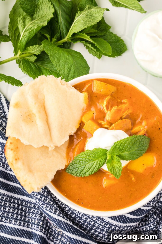 Delicious Indian Spiced Chicken Potato Stew in a white bowl, garnished with fresh yogurt, mint, and served with warm naan bread.