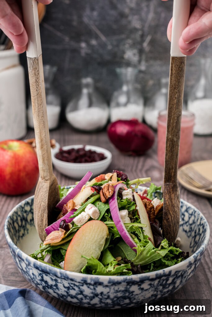 Thanksgiving salad being gently tossed with wooden salad tongs in a large bowl, combining all ingredients.