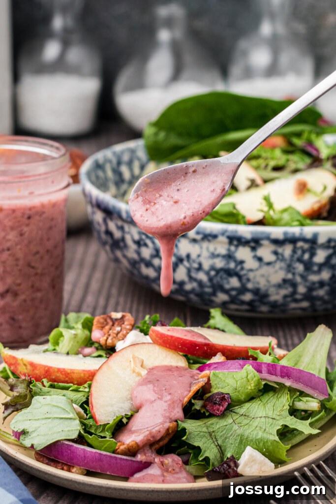 A stream of homemade cranberry vinaigrette salad dressing being poured from a spoon onto the vibrant Thanksgiving salad.