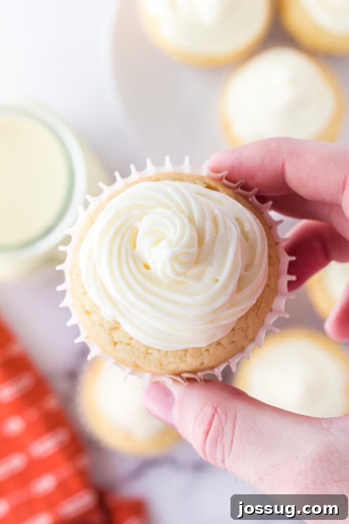 Festive Eggnog Cupcakes 3 A hand gently holds a perfectly frosted eggnog cupcake, showcasing its inviting texture and festive appeal against a warm backdrop.