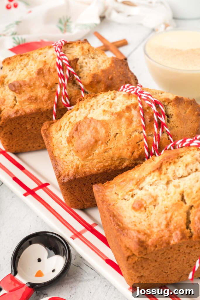 Three golden-brown loaves of Holiday Eggnog Bread lined up neatly on a patterned festive towel, signifying abundance and readiness for sharing.