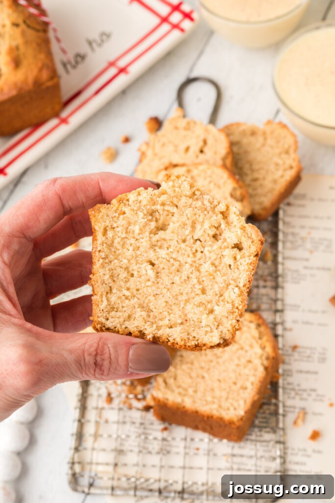 A hand gently holding a generous slice of golden-brown Holiday Eggnog Bread, ready to be savored and enjoyed as a festive treat.