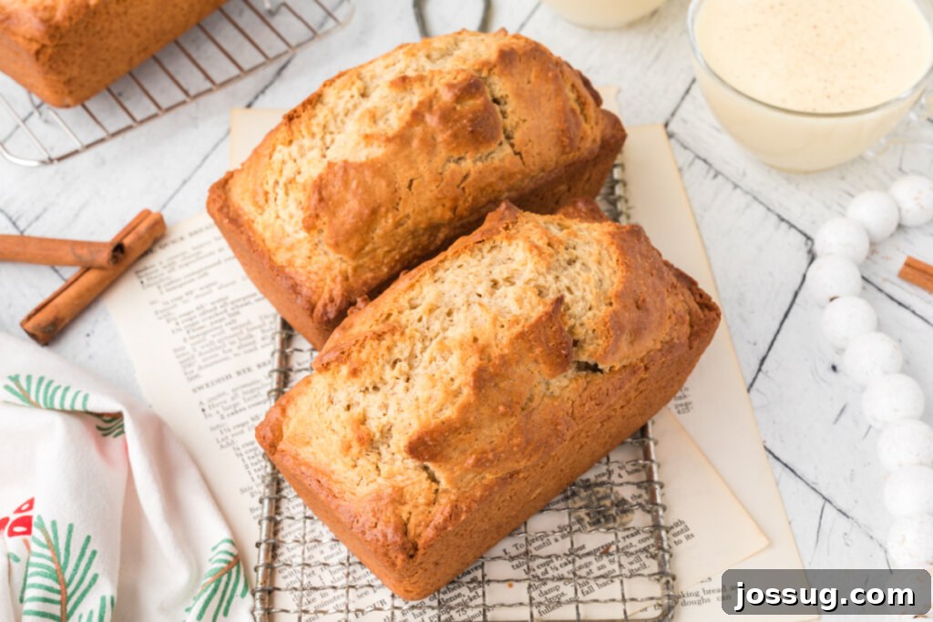 Two perfectly golden-brown loaves of finished Holiday Eggnog Bread resting on a cooling rack, showcasing their enticing crust and ready appearance.