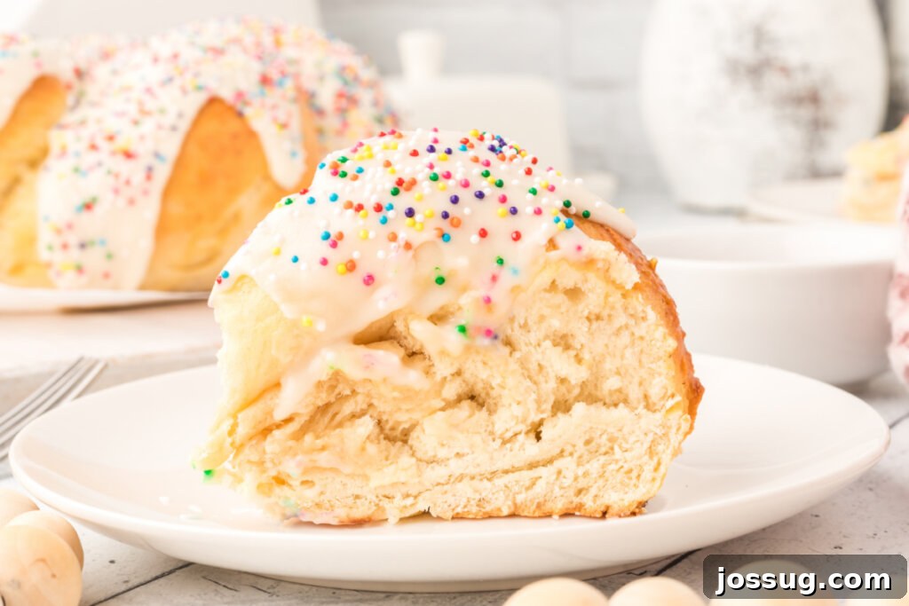 A solitary slice of frosted Italian anise bread, perfectly presented on a white plate, highlighting its delicate crumb and colorful nonpareil topping.