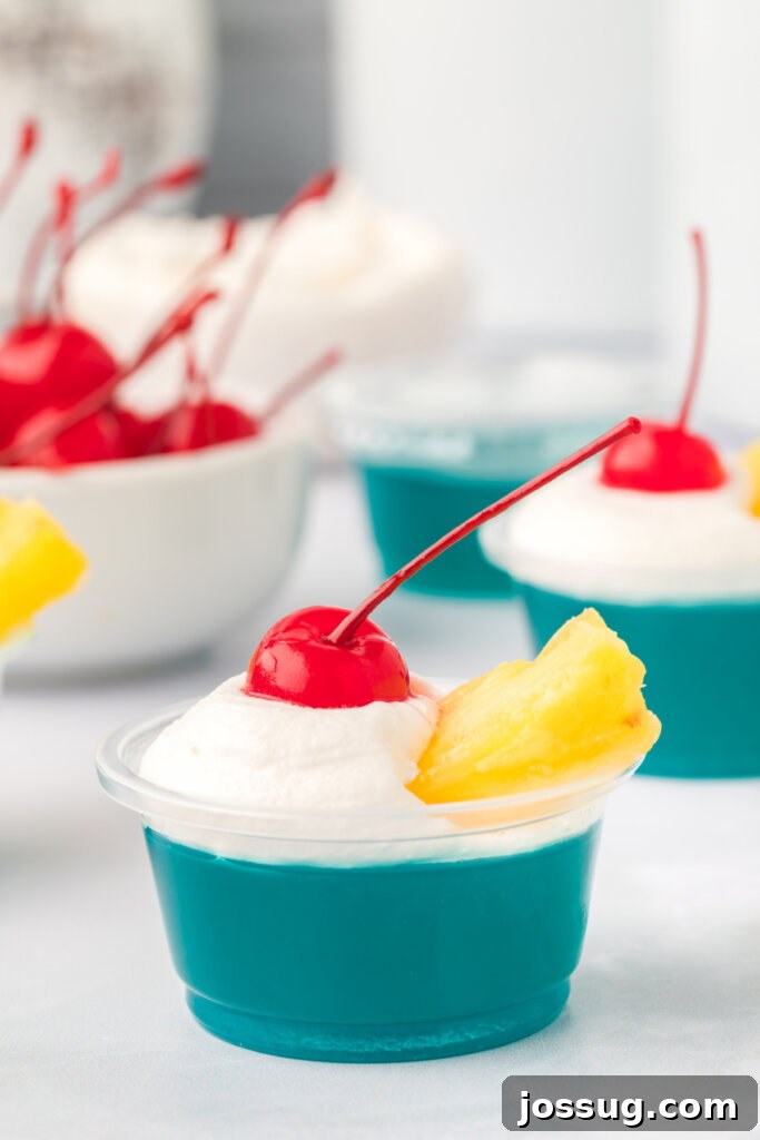 Aloha Glow Gels 3 A single Blue Hawaiian jello shot, elegantly topped with fluffy whipped cream, a juicy pineapple tidbit, and a vibrant maraschino cherry.