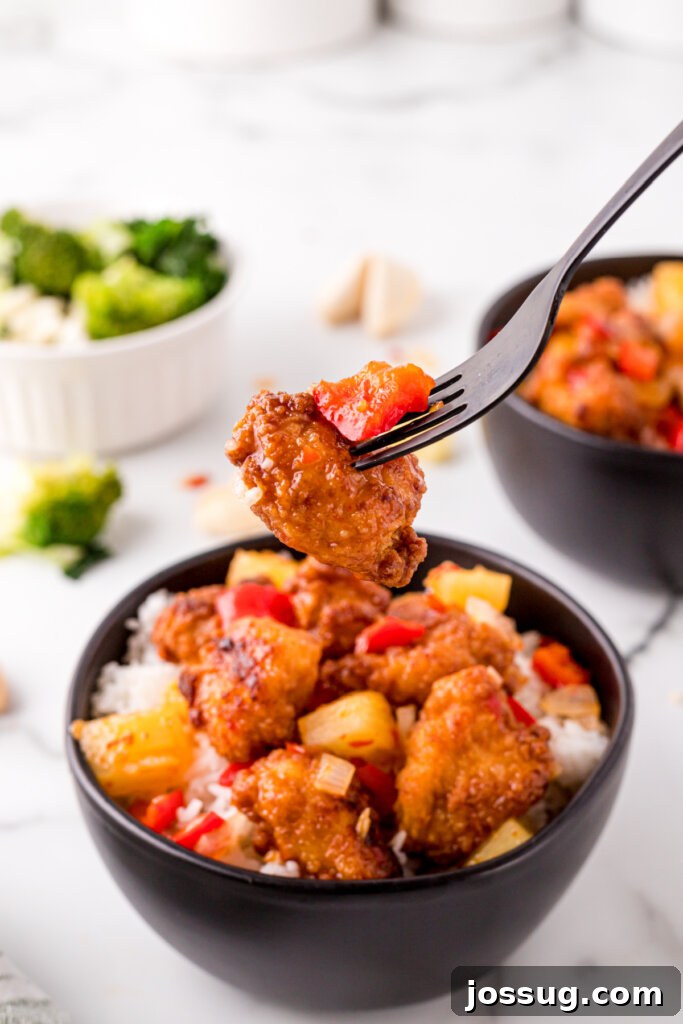 Tender Sweet Fire Chicken - A Bite of Flavor A fork lifts a piece of sweet fire chicken from a bowl, showing the juicy chicken and pineapple coated in sauce.