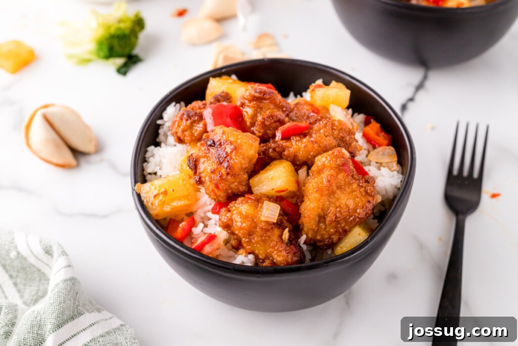 Satisfying Sweet Fire Chicken for the Whole Family A wide shot of a black bowl brimming with Copycat Sweet Fire Chicken, showcasing the abundance of chicken, pineapple, and peppers.
