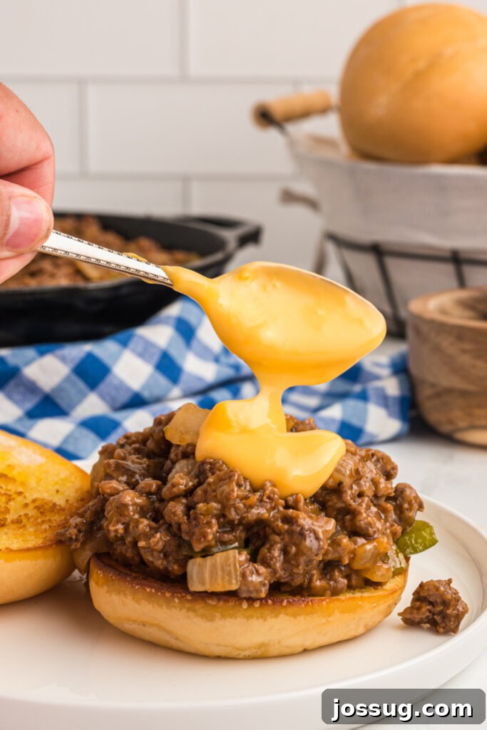 Philly Cheesesteak Sloppy Joe Twist 4 spooning melted cheese whiz onto the top of a philly cheesesteak sloppy joe