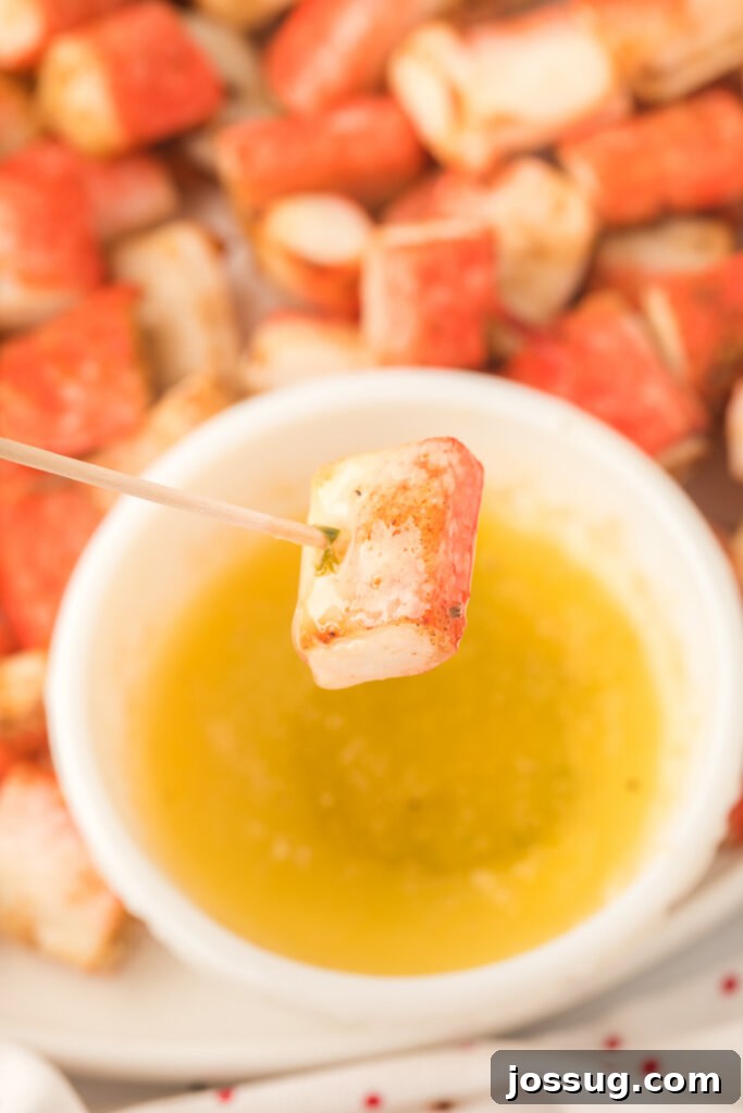 A crispy air fryer crab bite on a toothpick, poised over a small bowl of creamy garlic butter dipping sauce.