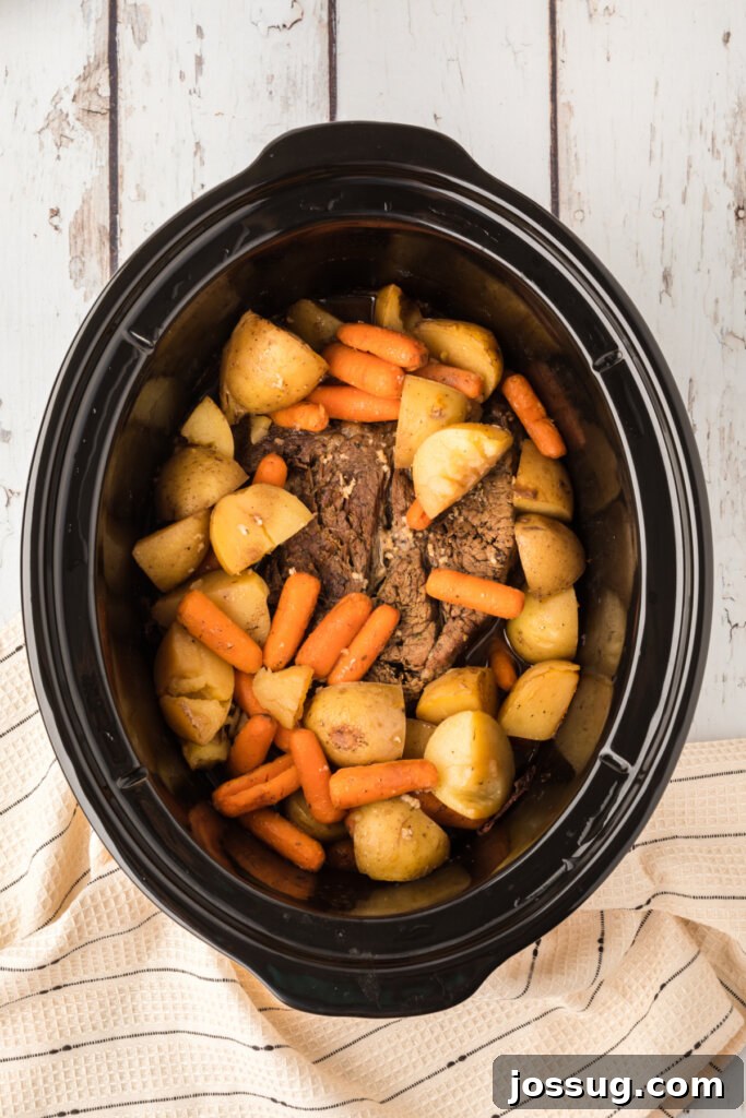 Timeless Pot Roast 3 Uncooked pot roast, potatoes, and carrots nestled together in a slow cooker, ready for the cooking process.