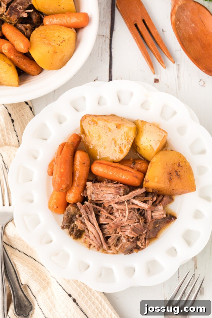 Timeless Pot Roast 5 A generous portion of shredded pot roast with tender potatoes and carrots on a white plate, ready to be enjoyed.