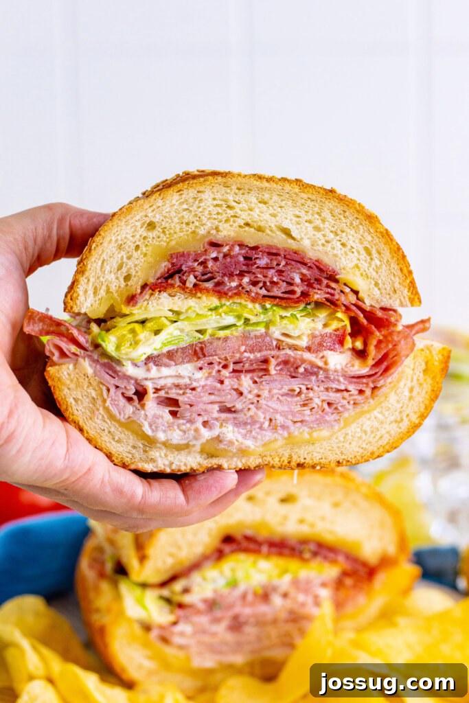 Hand holding a cross-section of a Grinder Salad Sub, showing the layers of meat, cheese, and salad.