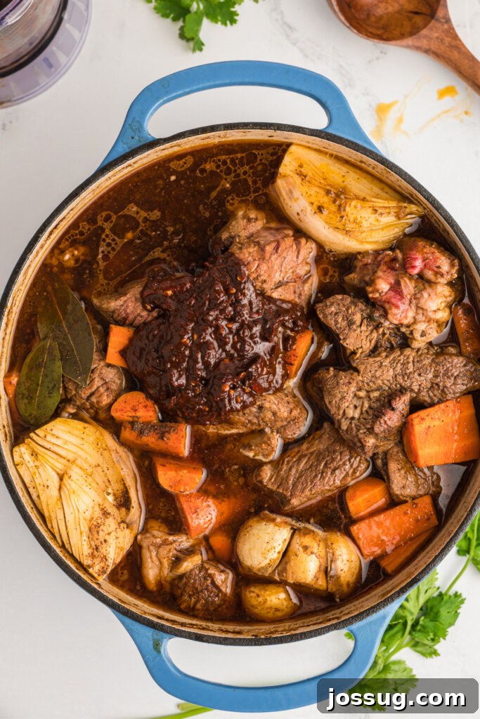 Dutch oven with birria stew meat, peppers, and vegetables simmering