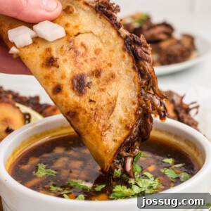 hand dipping birria taco into consommé