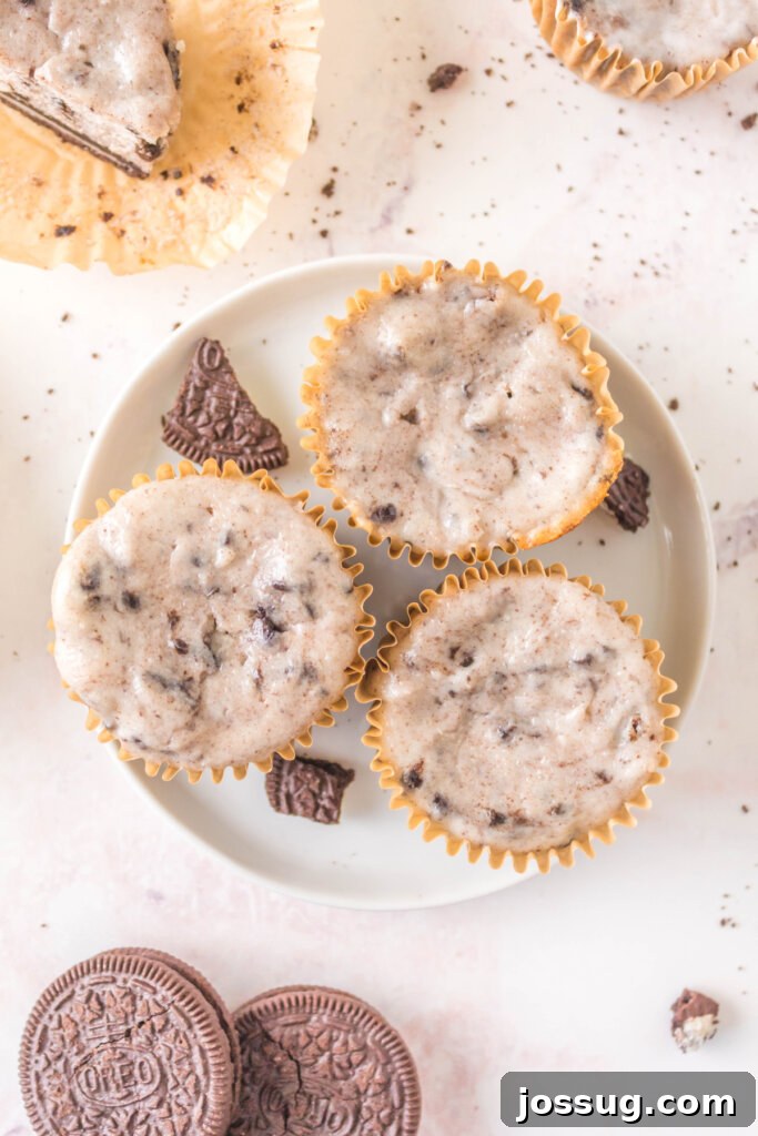 Three beautifully presented Oreo Cheesecake Cupcakes resting on a pristine white plate, adorned with a delicate topping, eagerly awaiting to be savored.