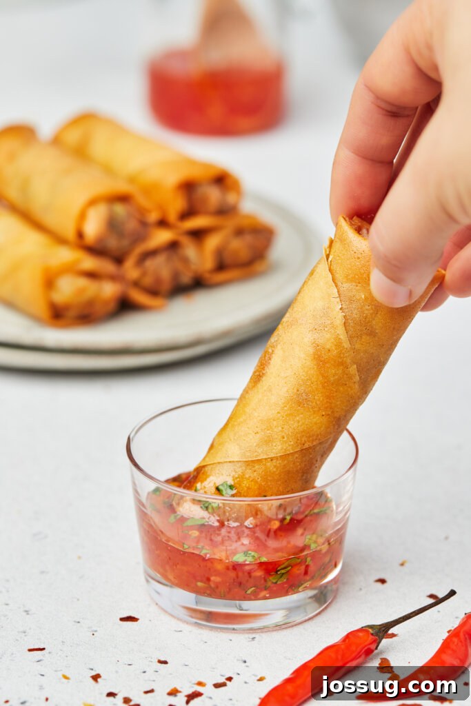 Hand dipping a crispy vegetable spring roll into sweet chili sauce