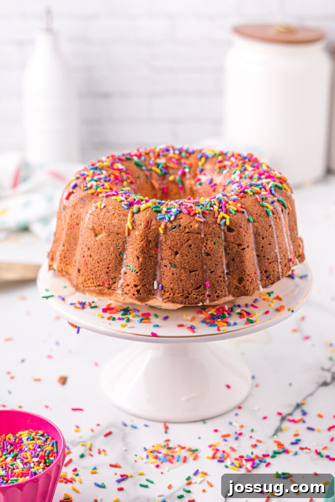 Rainbow Sprinkle Pound Cake 3 A whole Funfetti Pound Cake elegantly displayed on a white cake stand, showcasing its perfectly baked golden crust and the potential for joyful slices.