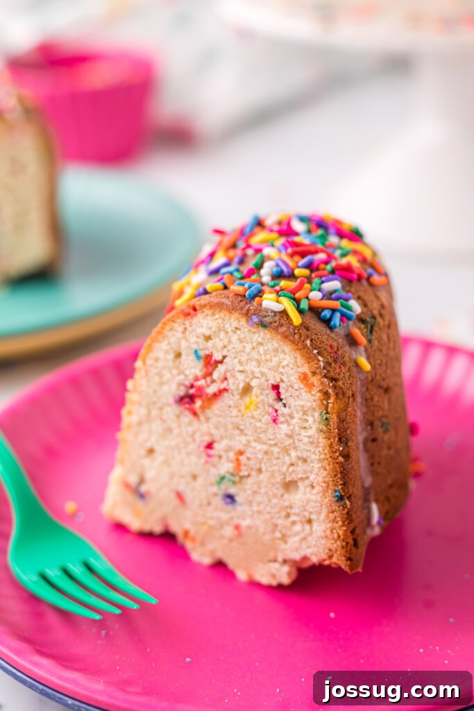Rainbow Sprinkle Pound Cake 5 A delightful slice of Funfetti Pound Cake served on a pink plate with a teal fork, ready to be enjoyed, highlighting its vibrant interior.